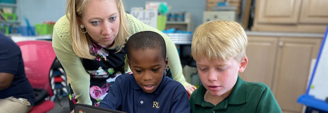 Teacher helping two students with chromebook