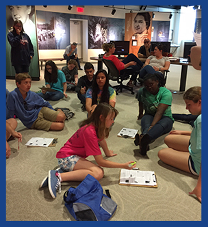 Students using clip boards to complete a group project as they sit on the floor